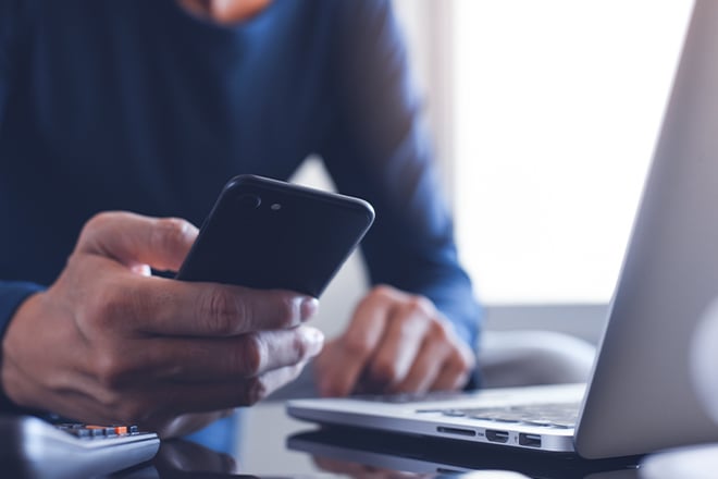 Close up of a person looking at their phone with their laptop beside them