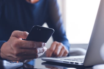 Close up of a person looking at their phone with their laptop beside them