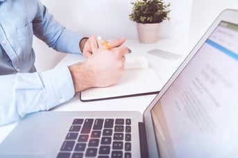 Close up of a person taking written notes while sitting next to their laptop