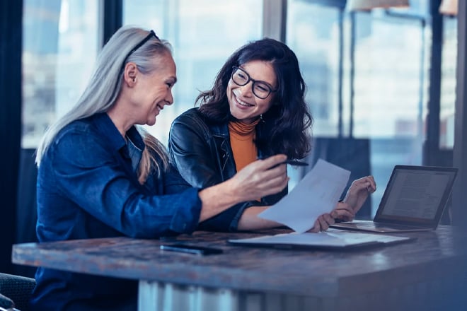 Two coworkers smiling and laughing while discussing work in a conference room