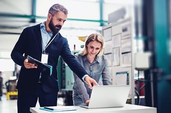 A portrait of an industrial man and woman engineer with laptop in a factory, working.