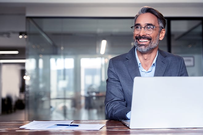 Middle-age businessman smiling while typing on his computer looking aside
