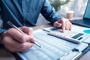 Person using calculator and reviewing financial documents for accounting and budget planning