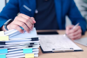 Business professional reviewing and organizing stack of documents with laptop