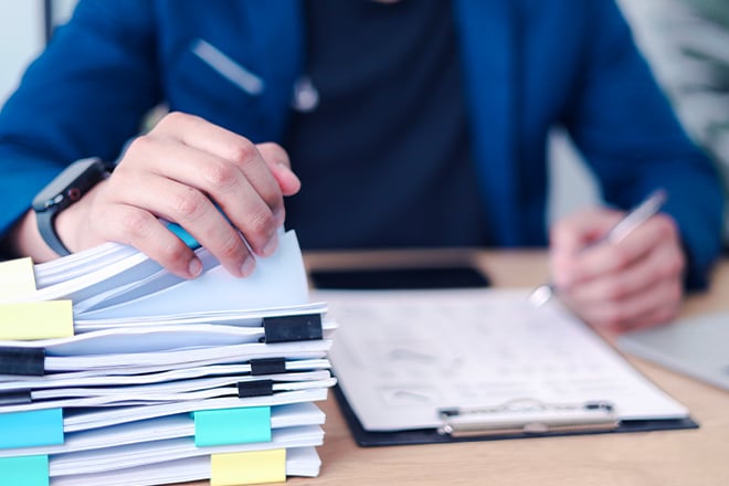 Business professional reviewing and organizing stack of documents with laptop