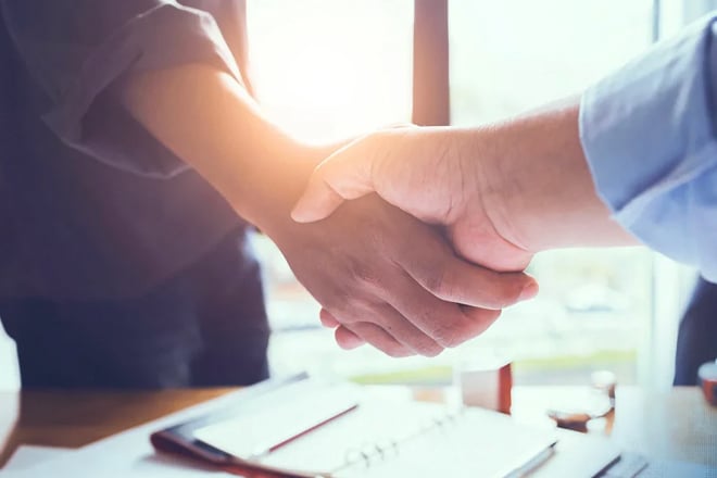 Two business professionals shaking hands over desk with documents