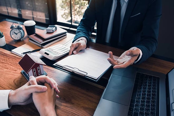 Real estate agent with calculator and house model discussing documents with client
