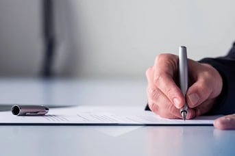 Hand signing contract document with pen on desk