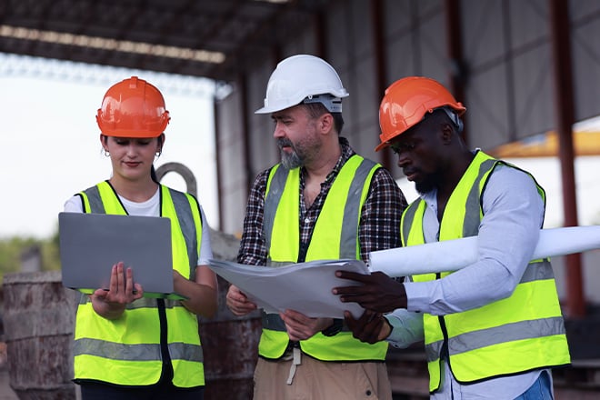 Construction workers in hard hats and safety vests reviewing plans at job site