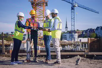 Team of General Contractor and Subcontractors look at a tablet while on a construction site.
