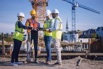 Team of General Contractor and Subcontractors look at a tablet while on a construction site.