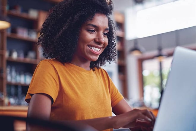 Woman in yellow shirt smiling while working on laptop
