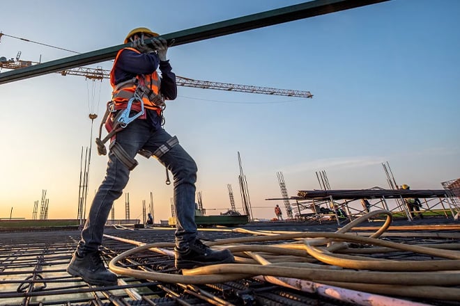 Construction worker in safety harness walking on steel beams at height