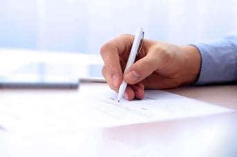 Hand holding pen preparing to sign document on desk