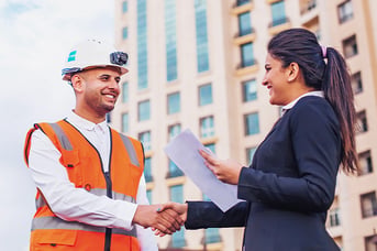 Construction worker in safety vest shaking hands with business professional outdoors