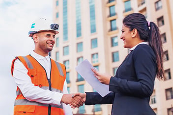 Construction worker in safety vest shaking hands with business professional outdoors