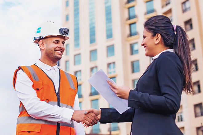 Construction worker in safety vest shaking hands with business professional outdoors