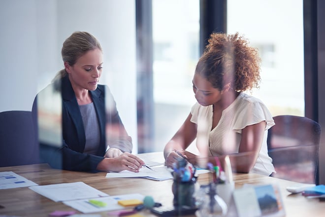 Two women sitting in an office looking at compliance documents together.