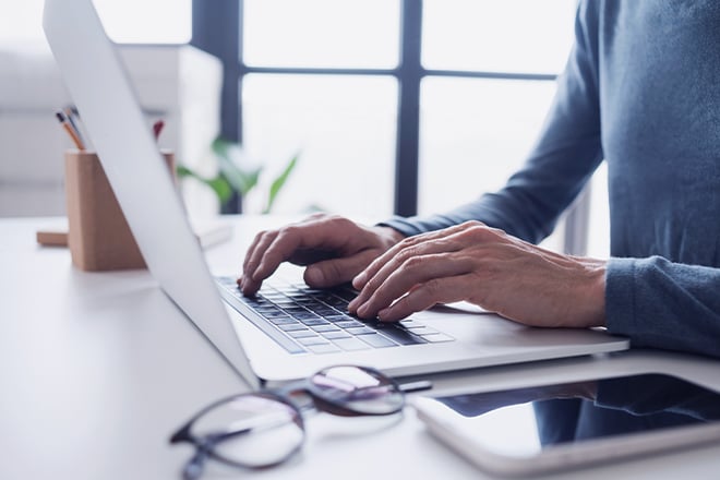 Person typing on laptop at desk with glasses and smartphone nearby