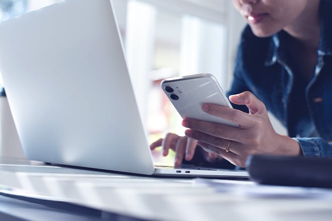 Close up of young business woman working on laptop computer and using mobile phone.
