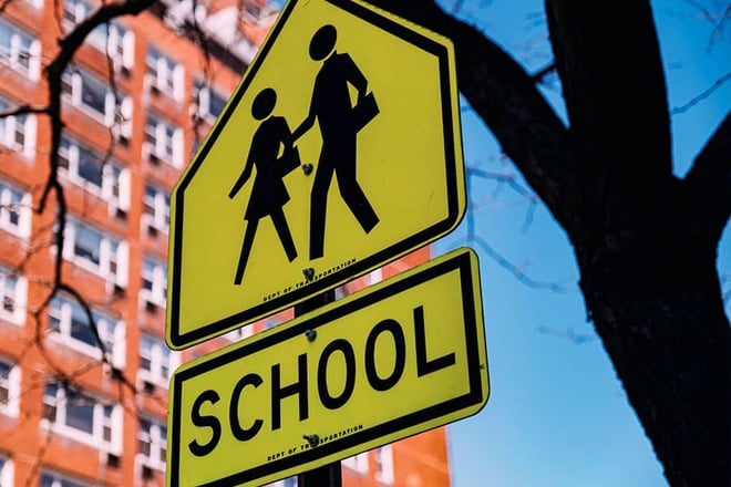 Road sign signifying a school with high-rise building in the background.