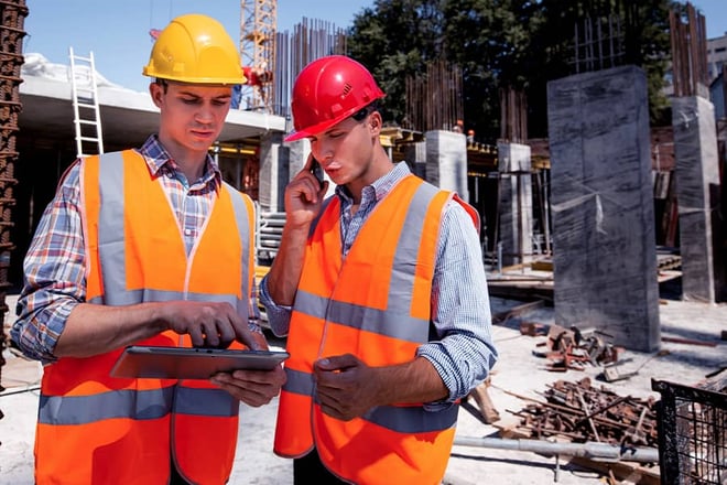 Two contractors reviewing information on a tablet while on a job site.
