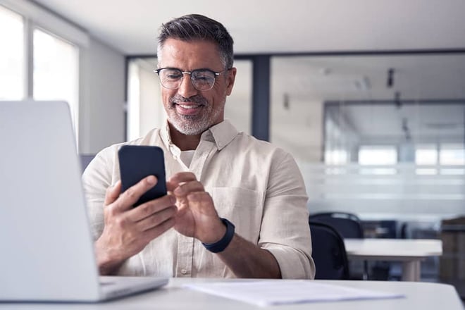 A business man in an office smiling while looking at his smartphone.