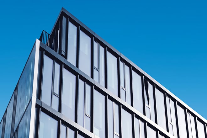 A modern white building with large rectangular windows and black frames rises against a clear blue sky.