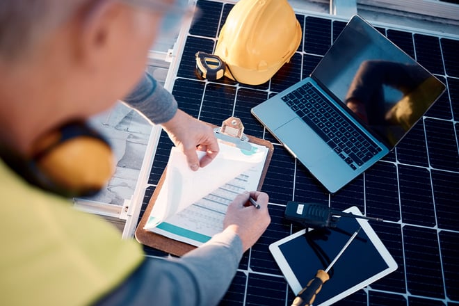 Over the shoulder view of a manager on a solar power construction site reviewing insurance paperwork.