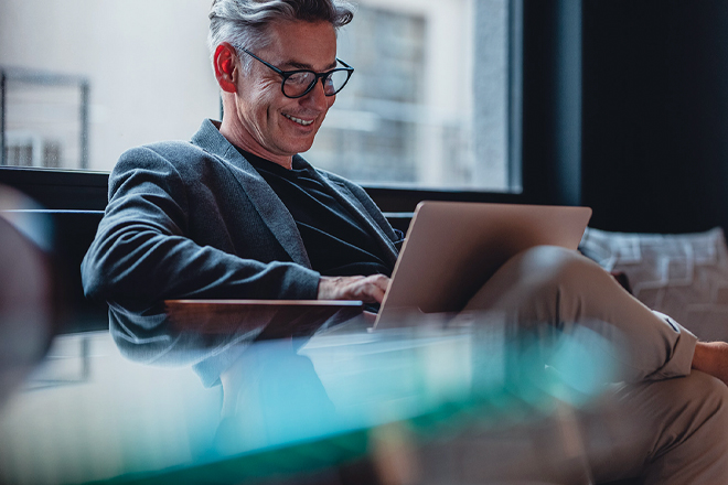 A businessman with gray hair smiling while looking at his laptop in his office