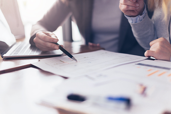 Close up of two employees reviewing documents line by line with a pen