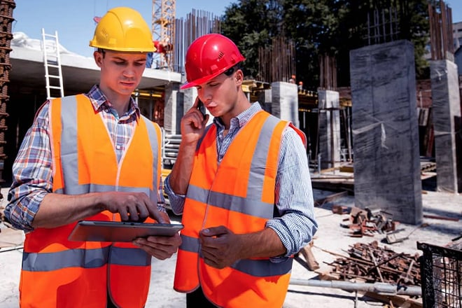 Construction workers in hard hats and safety vests reviewing tablet on site