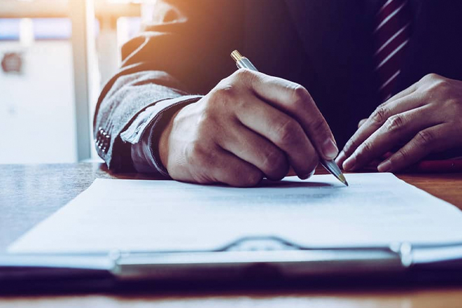Business person signing document with pen at desk
