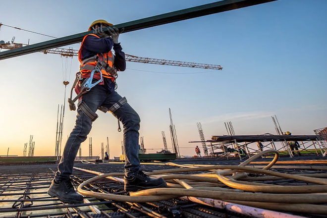 Construction worker in safety harness walking on steel beams at height