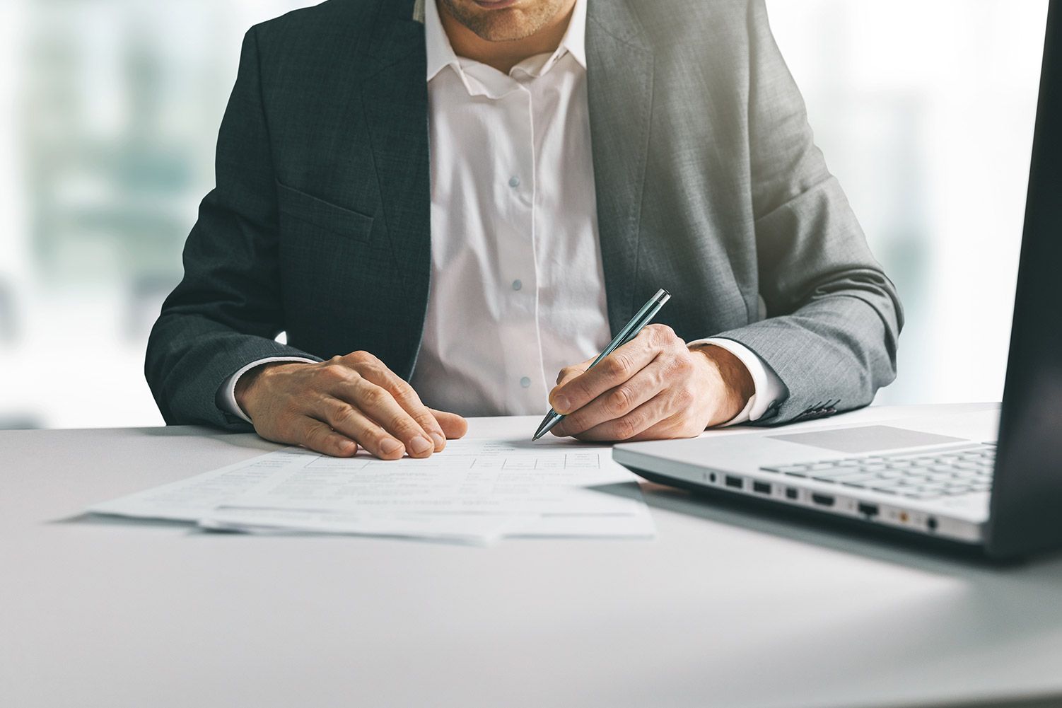 Man in suit writing business papers at desk in office