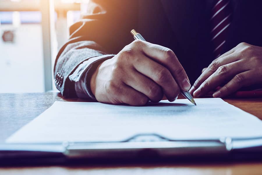 A close up a person writing on a piece of paper on a clipboard.