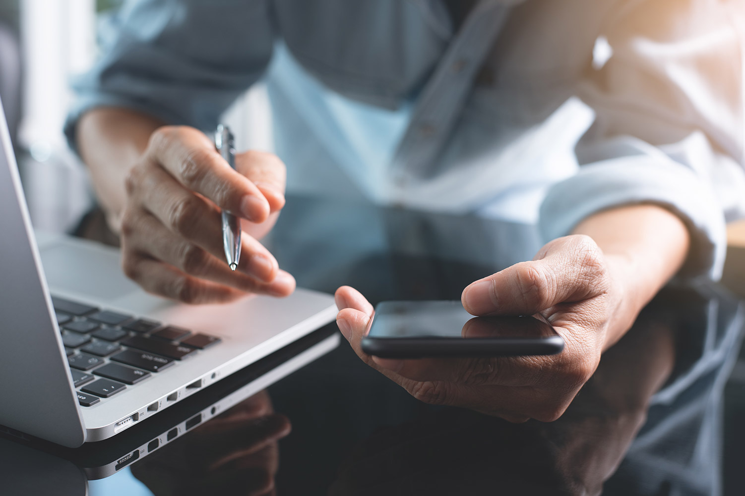 man holding phone and pen in front of laptop