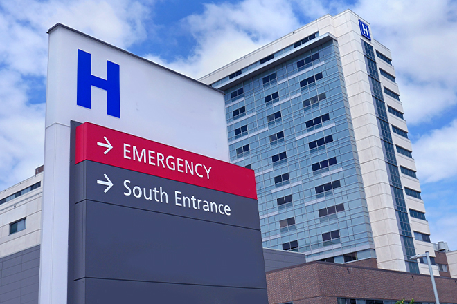 Modern hospital building with directional signs pointing to Emergency and South Entrance