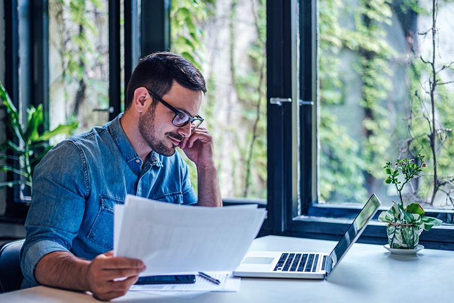Male entrepreneur or businessman reading information on a laptop and printed documents