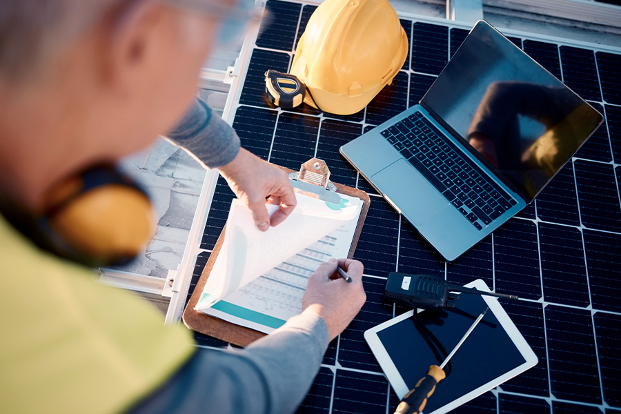 Over the shoulder view of a manager on a solar power construction site reviewing insurance paperwork.