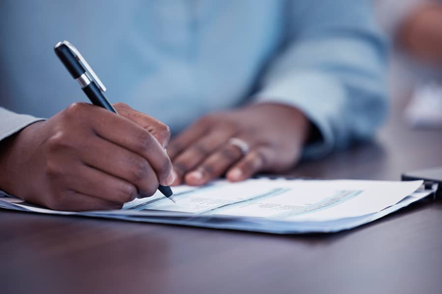Close up of a person signing paperwork.