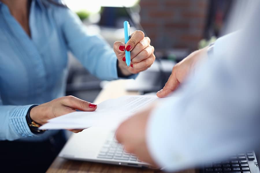 A closeup of two people exchanging signed documents in an office setting.