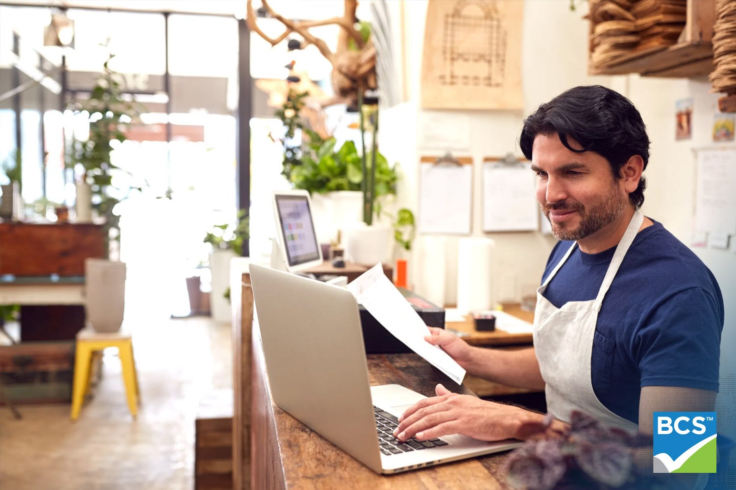 business shop owner working on laptop with papers in hand