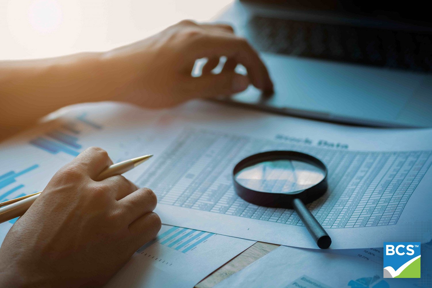 man looking at documents with magnifying glass sitting on top of financial documents