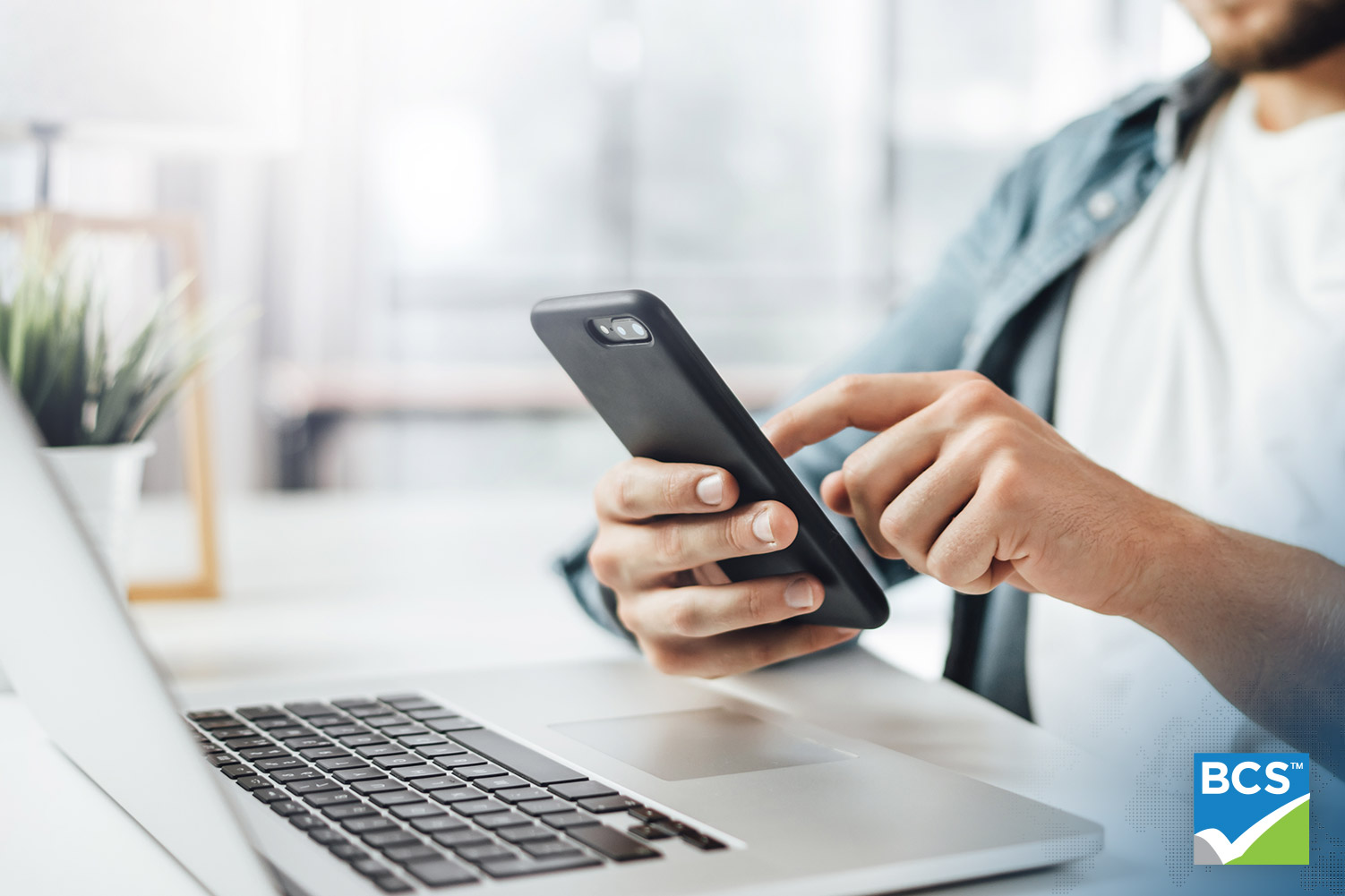 man using cellphone and laptop sitting at a desk