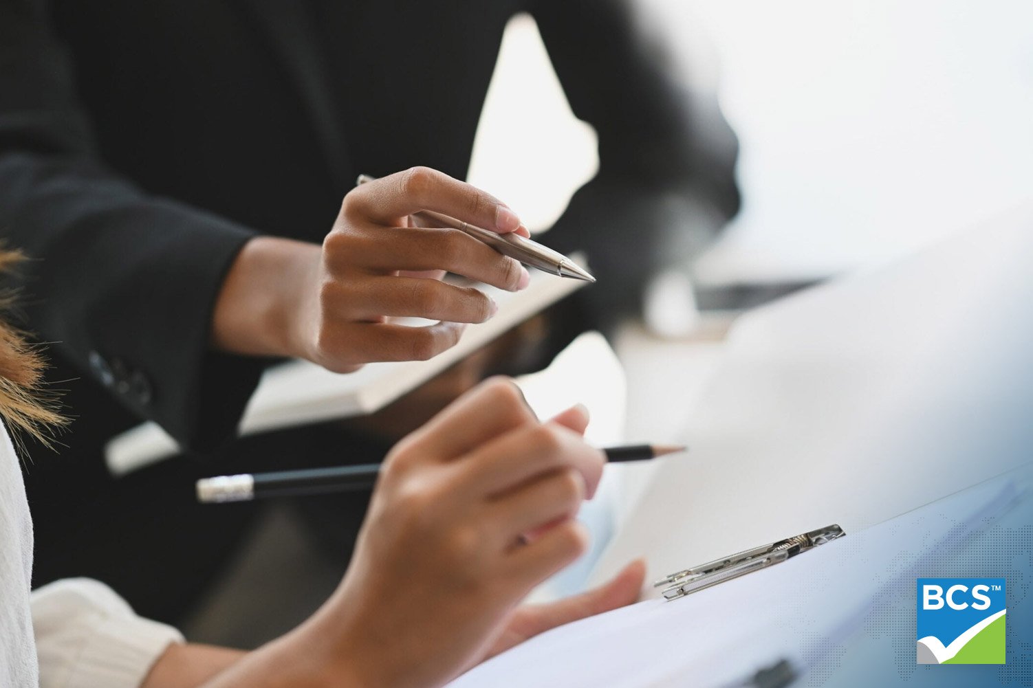 Two people holding a pen and pencil while looking at a printed document.