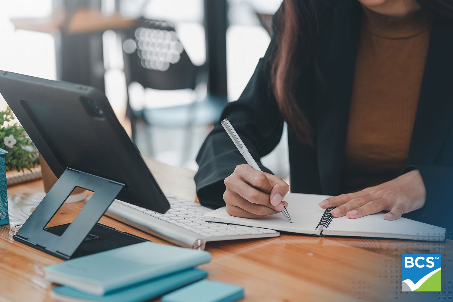 woman writing in notebook and looking at tablet at desk