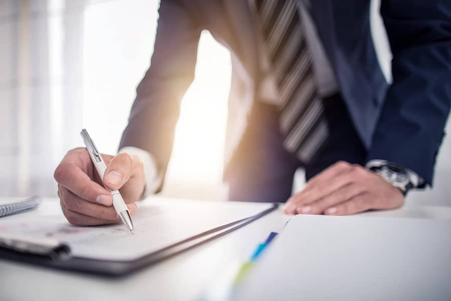 man in suit leaning over desk filling out paperwork