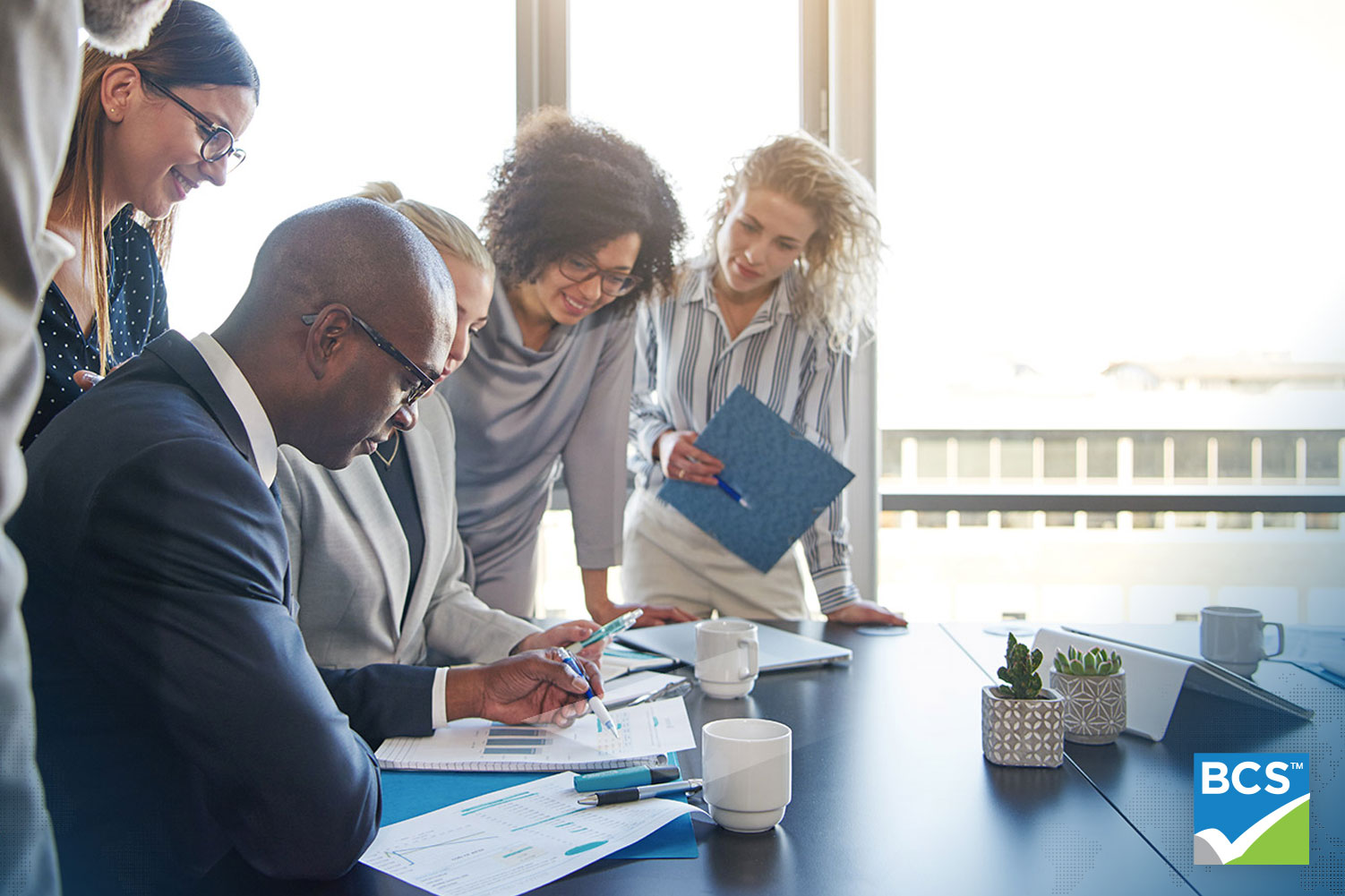 group of people working over a desk that is messy with papers all looking at the same thing