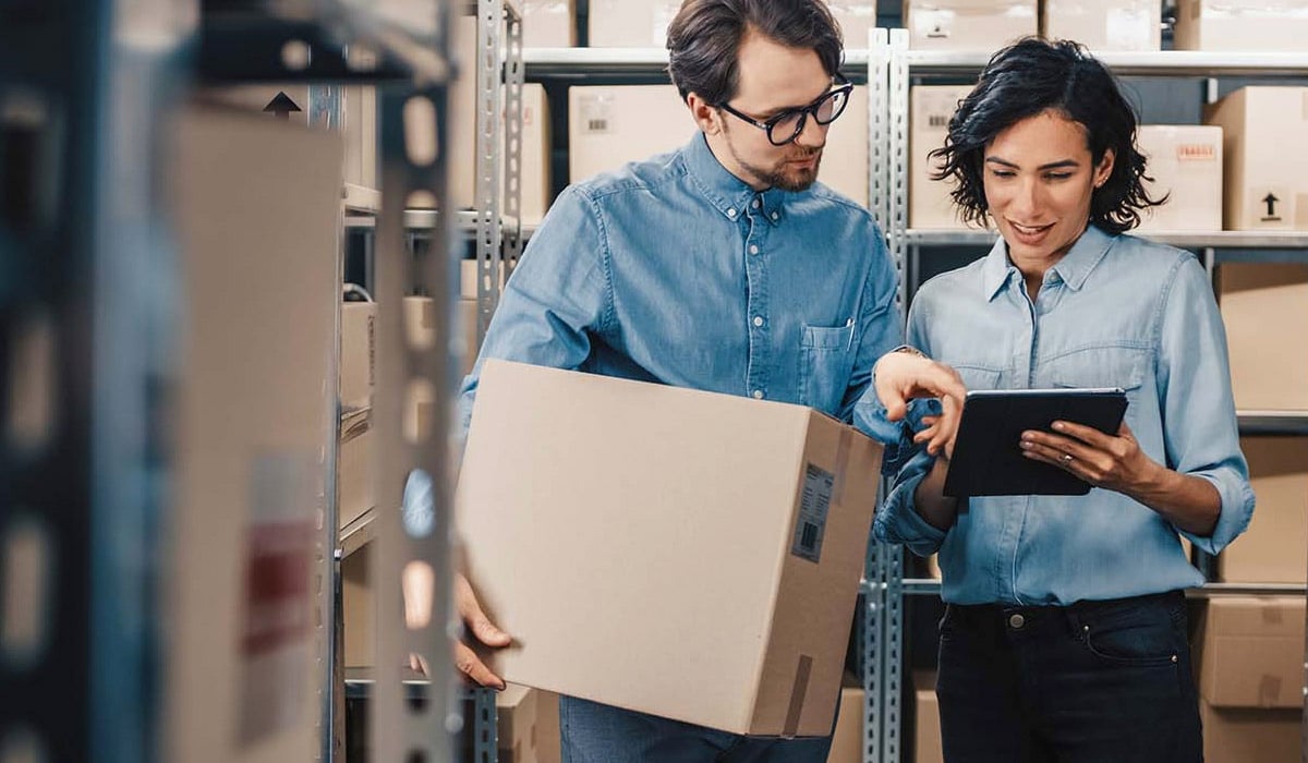 man-and-woman-looking-at-tablet-in-warehouse-setting man-and-woman-looking-at-tablet-in-warehouse-setting